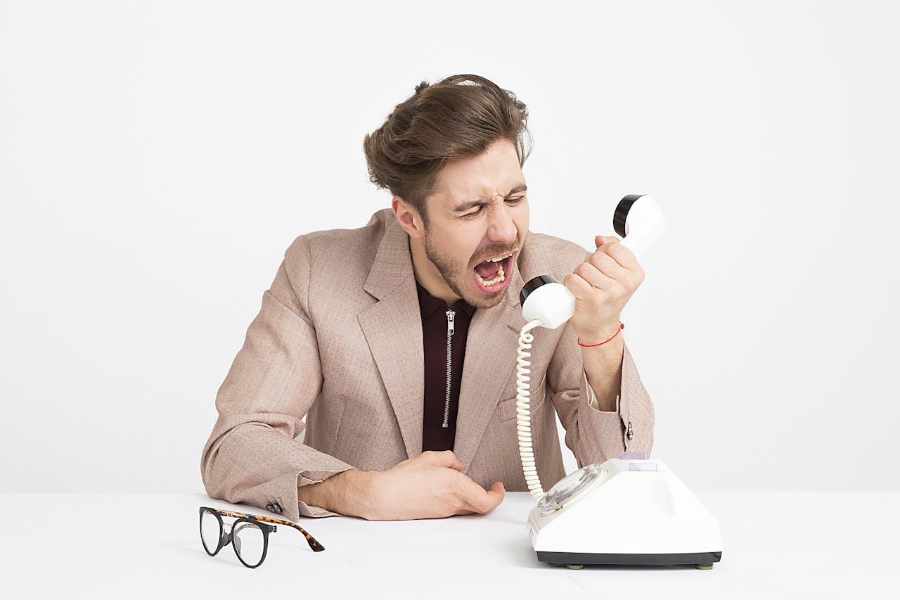 In foto, una persona che urla alla cornetta del telefono.