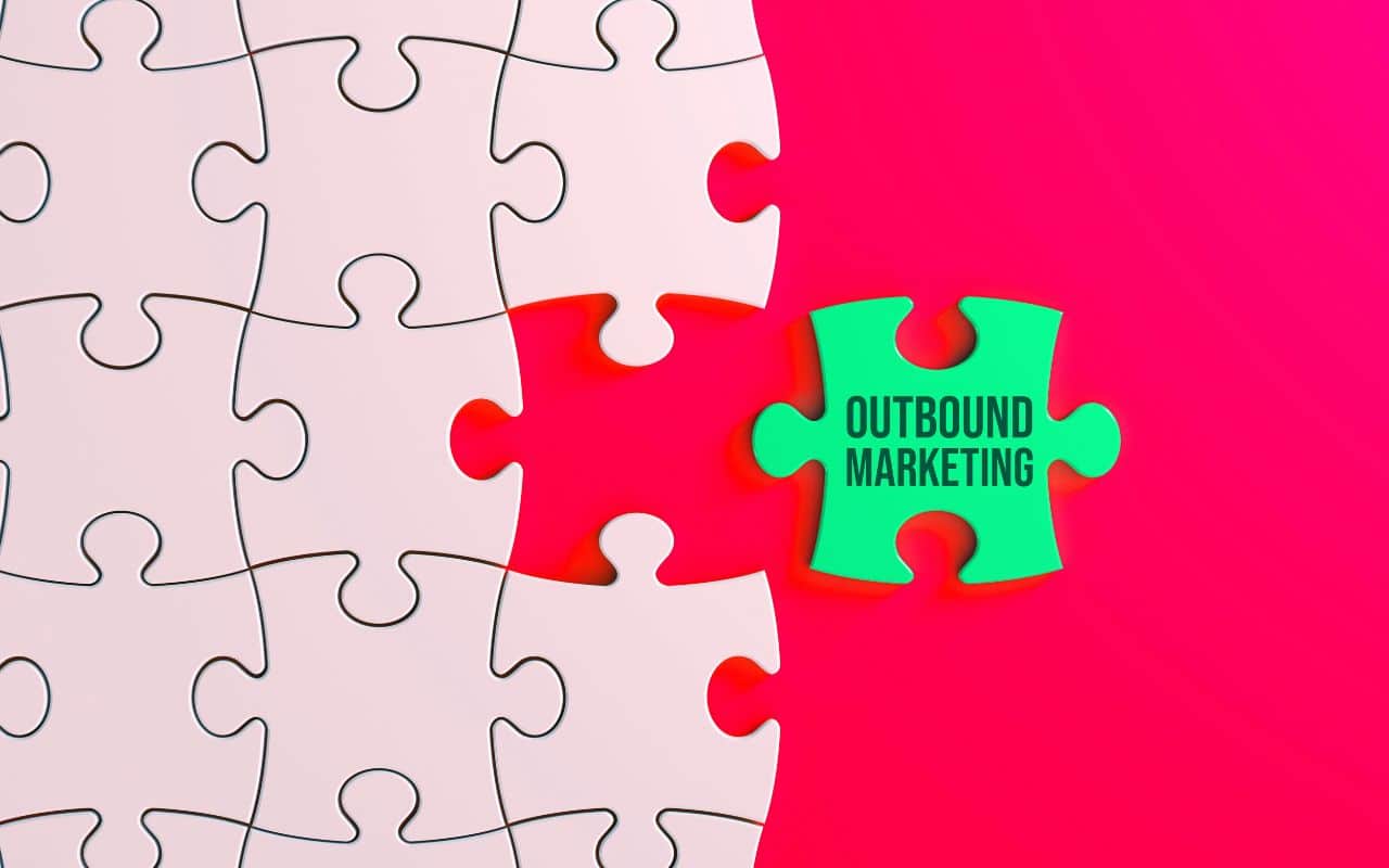 Un'immagine di un puzzle incompleto con uno sfondo rosa. Un pezzo verde del puzzle, separato dagli altri, mostra il testo "OUTBOUND MARKETING".