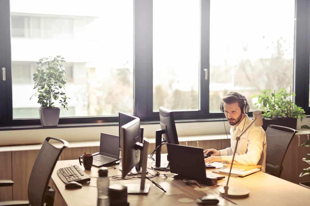 Operatore di call center con cuffie lavora al computer in un ufficio moderno con luce naturale, gestendo lead e comunicazioni digitali.