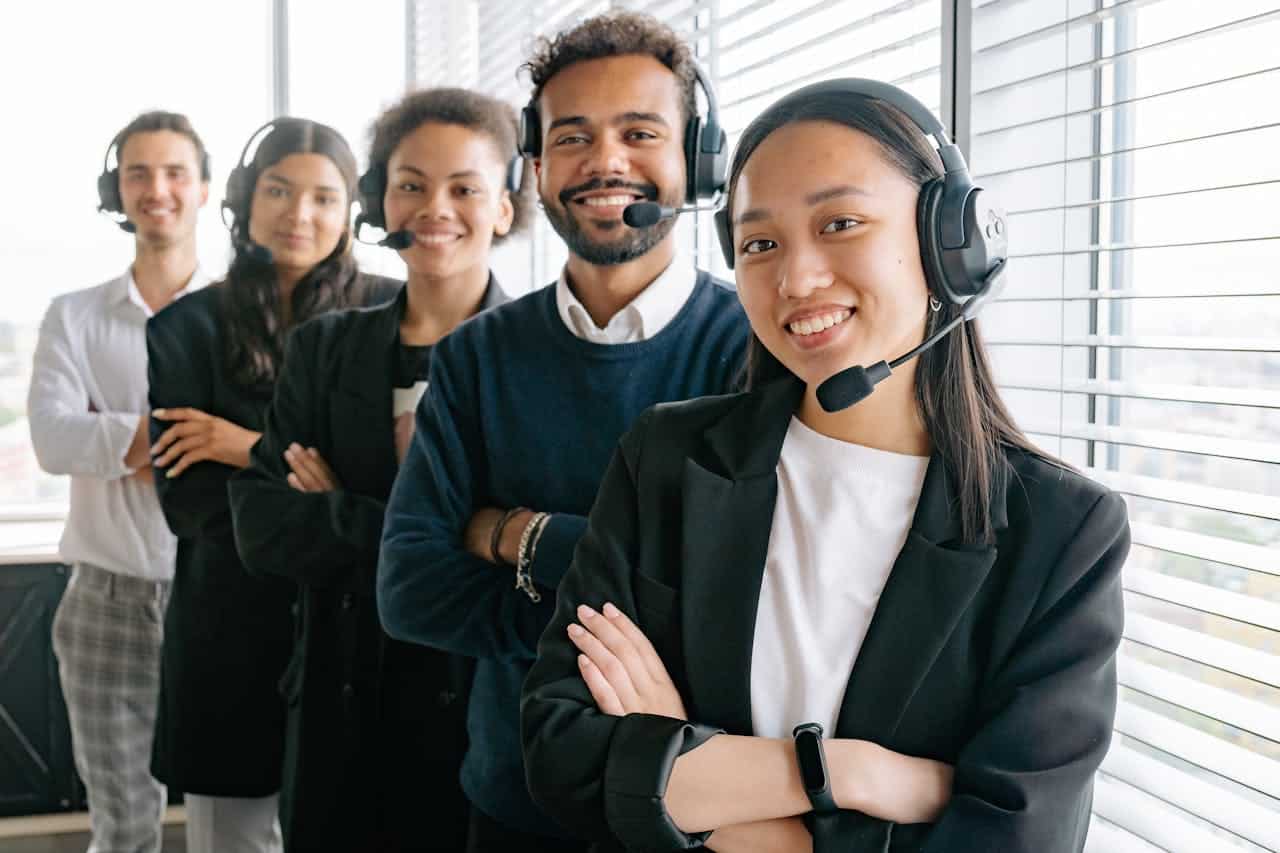 Team di operatori di un call center digitale con cuffie e microfono, sorridenti e pronti a offrire assistenza clienti in un ufficio moderno.