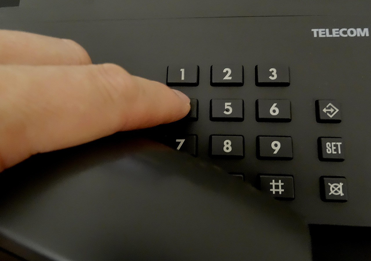 Mano che digita su tastierino telefonico di un telefono fisso Telecom, simbolo di attività outbound in un call center.