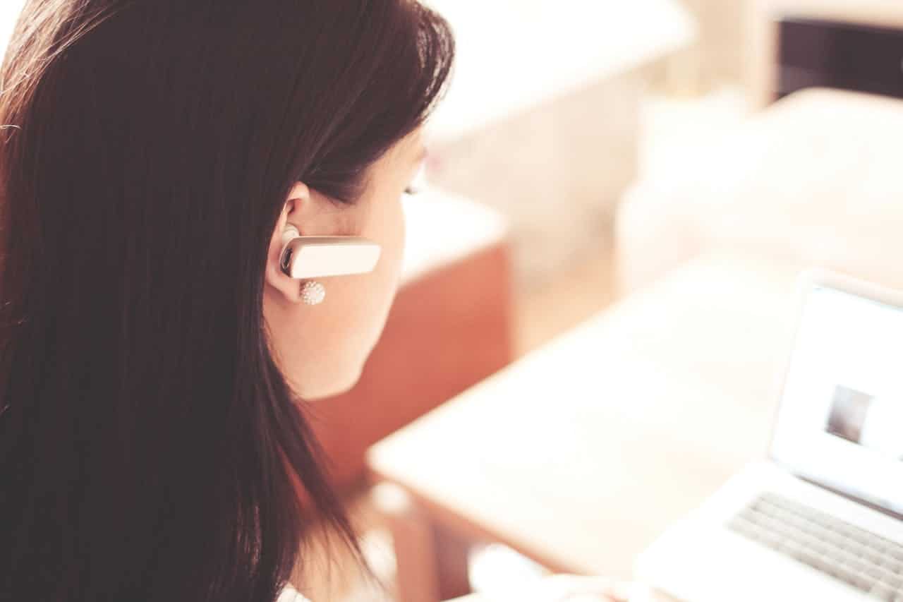 Operatrice call center con auricolare wireless davanti al laptop, durante una sessione di assistenza clienti inbound.